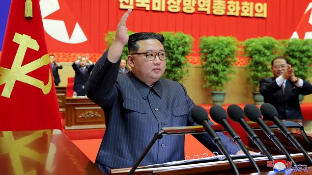 Kim Jong-un lève la main derrière son lutrin.