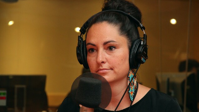 Une femme portant un casque d'écoute et des boucles d'oreilles autochtones est derrière un micro.