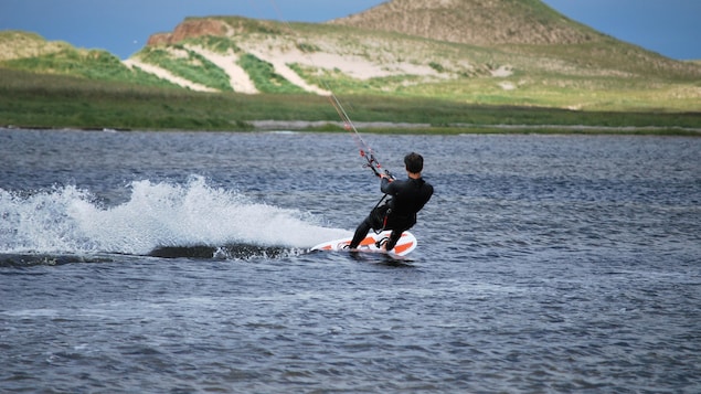 Un homme fait du kitesurf sur l'eau avec une montagne verdoyante à l'arrière.
