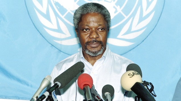 Kofi Annan est en conférence de presse; le drapeau de l'ONU est affiché derrière lui.