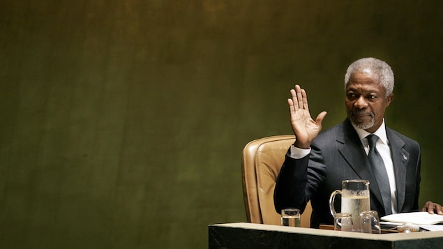 Kofi Annan est assis à un bureau et fait un signe de la main.
