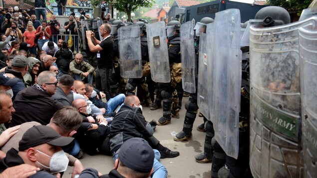 Des manifestants sont assis sur la chaussée en face d'une rangée de policiers antiémeutes.