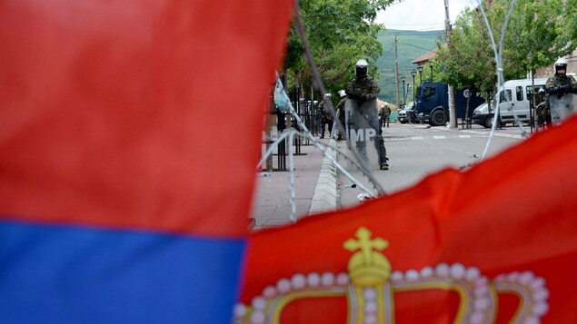 Un soldat se dresse derrière des fils barbelés sur lesquels sont posés des drapeaux de la Serbie.