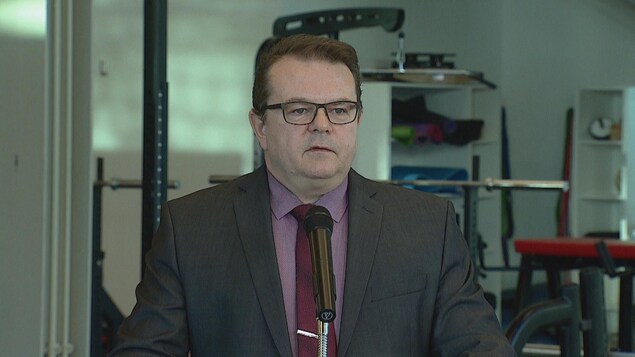 Kyle Ripley se tient à un podium devant une salle de conditionnement physique. Kyle Ripley se tient à un podium devant une salle de conditionnement physique.