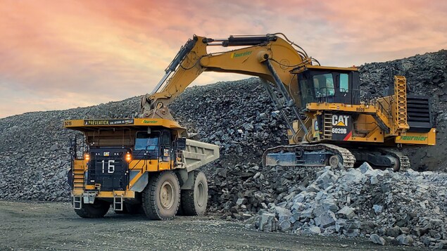 Dans une mine à ciel ouvert, une pelle dépose de la roche dans un camion.
