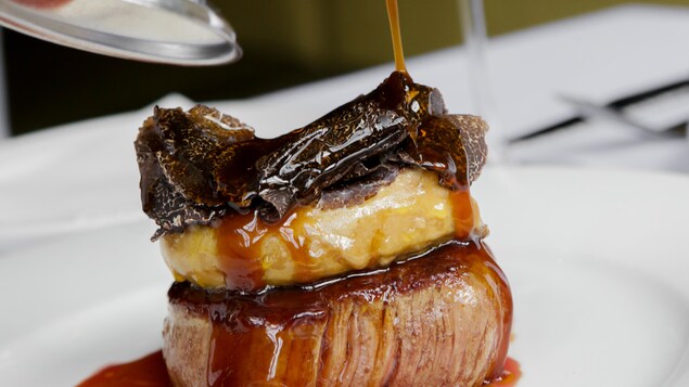 Un morceau de viande sur une assiette avec un verre de vin rouge en arrière-plan.