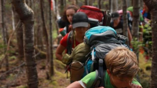 Des enfants marchent en forêt avec des sacs d'expédition au dos.