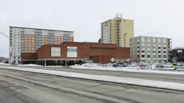 L'édifice de La grande place, près d'un stationnement et d'autres immeubles du centre-ville de Rimouski.