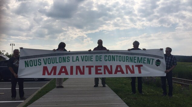 Des citoyens de Lac-Mégantic tiennent une pancarte qui réclame une voie de contournement le plus rapidement possible.