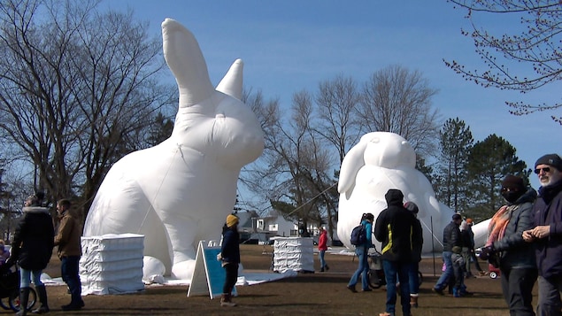 Des curieux observent des lapins géants gonflables dans un parc, au printemps.