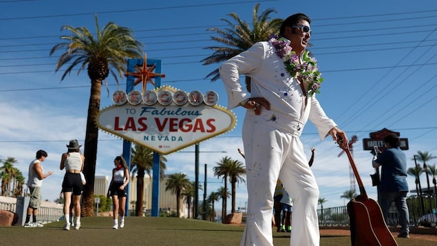 An Elvis impersonator holding a guitar in front of a Las Vegas sign.