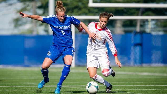 Sur le terrain, la joueuse de soccer Laura Chénard se dispute le ballon avec une adversaire. Sur le terrain, la joueuse de soccer Laura Chénard se dispute le ballon avec une adversaire.