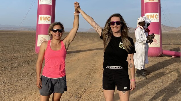 Deux femmes souriantes avec les bras dans les airs dans le désert marocain.