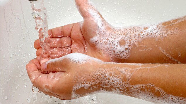 Les mains savonneuses d'un enfant sous l'eau d'un évier.