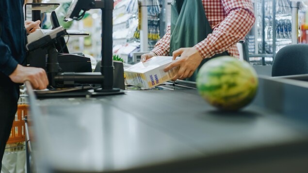 Un employé d'une épicerie scanne les achats d'un client, dont un melon d'eau.