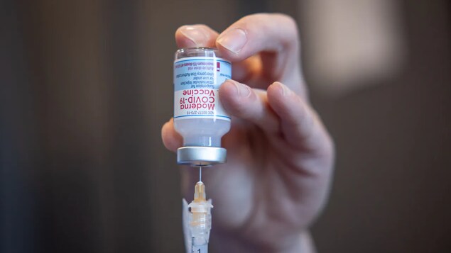 Une main tient une dose du vaccin Moderna et y insère l'aiguille.