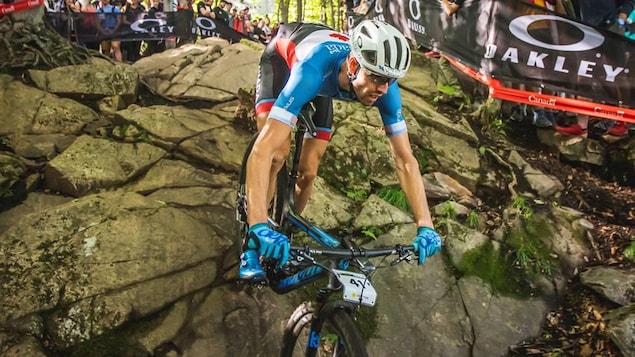 Le cycliste Léandre Bouchard descend une pente dans un sentier se trouvant dans une zone boisée.