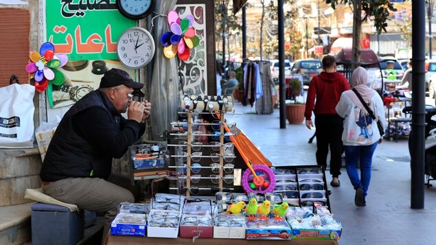 Salah Nasab, a Lebanese street vendor who also sells and repairs clocks, sits next of two clocks that show different times in Lebanon, in the southern port city of Sidon, on Monday. (Mohammed Zaatari/The Associated Press)