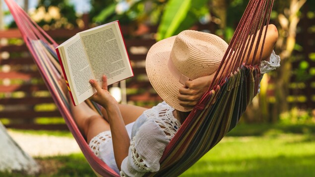 Une femme avec un chapeau lit un livre dans un hamac.