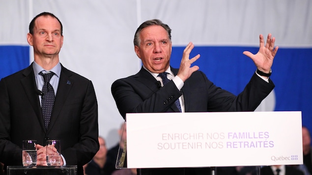Le ministre québécois des Finances, Eric Girard, et François Legault se tiennent derrière un podium.
