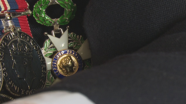 Un gros plan sur la médaille, accrochée sur le veston noir d'un vétéran.