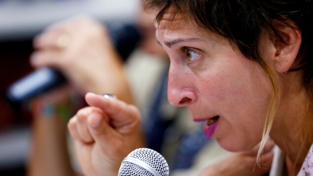 Une femme parle dans un micro, on la voit de profil.