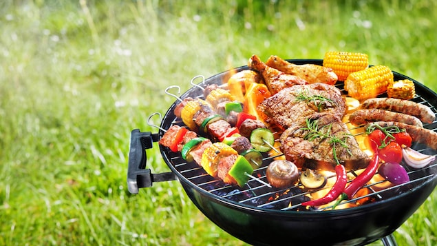 Des légumes, de la viande, des saucisses et des brochettes sur un barbecue au charbon.