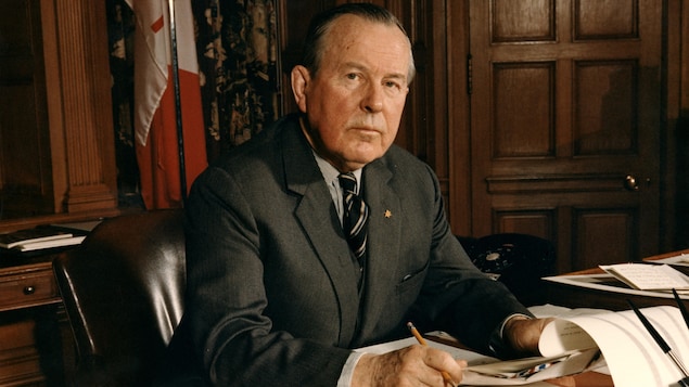 Assis à son bureau de premier ministre, le politicien Lester B. Pearson, tient des papiers dans ses mains.
