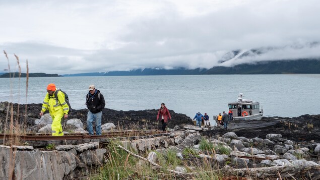 Un groupe de personne débarque d'un petit bateau de pêche, au fond l'océan et la côte, en Alaska, juillet 2022.
