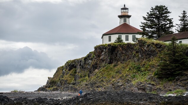 Le phare Eldred Rock en contre-plongée avec le récif et une personne qui marche sur la plage, en Alaska, juillet 2022.