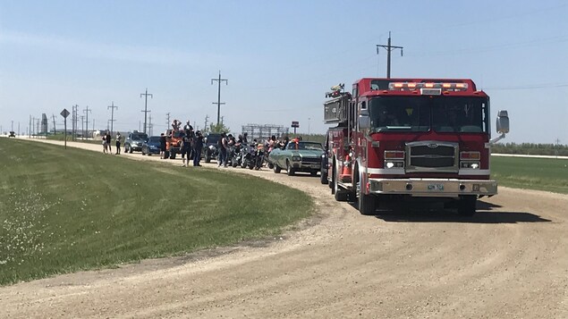 Des voitures et des motos en ligne qui roulent sur une route de terre.
