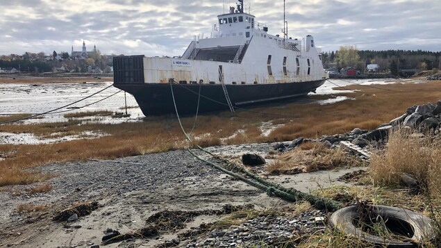 Le navire amarré dans une baie, à marrée basse. En arrière-plan, la ville de Trois-Pistoles.