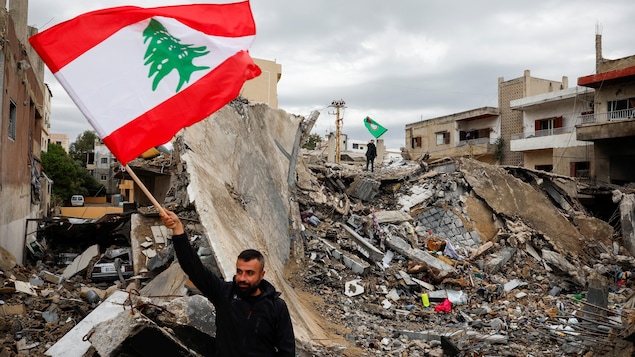 Un homme brandissant le drapeau libanais devant un immeuble anéanti par un bombardement israélien dans la ville de Tyr, dans le sud du Liban, le 27 novembre 2024.