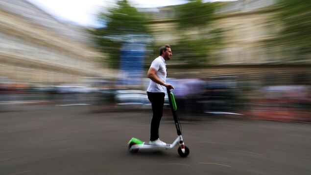 Un homme conduit une trottinette électrique de marque lime dans la rue.