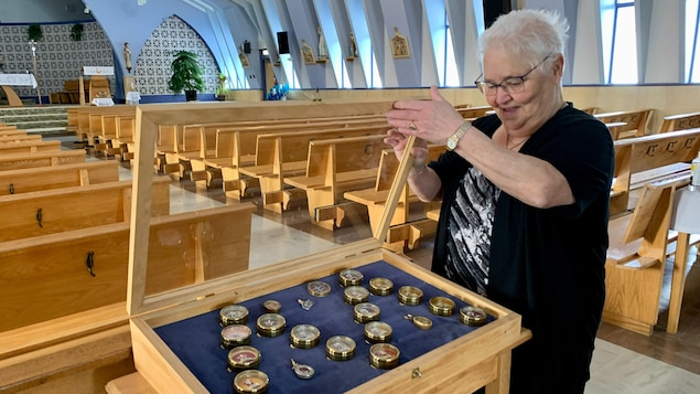 Lina Cormier ouvre le couvercle protecteur pour montrer les reliques d'apôtres exposées dans l'église.
