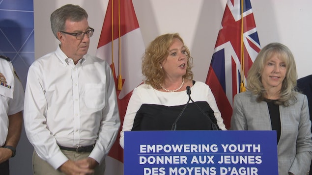 Jim Watson (à gauche), Lisa MacLeod (au centre) et Merrilee Fullerton (à droite) derrière un podium avec un micro pendant un point de presse.