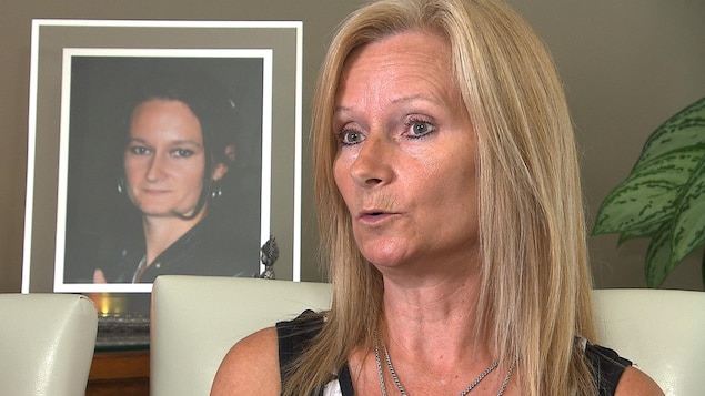 Lise Castonguay est assise sur une chaise blanche, devant une photo de sa fille Isabelle Lavoie, placée sur un meuble.