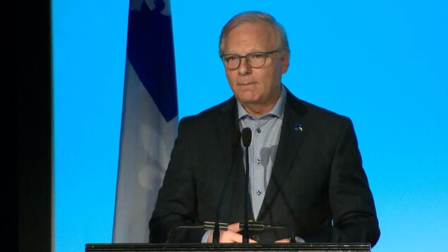 Jean-François Lisée se tient au lutrin avec un drapeau du Québec derrière lui. Jean-François Lisée se tient au lutrin avec un drapeau du Québec derrière lui.