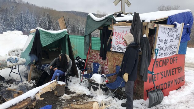 Une femme est assise et un homme se tient debout au campement érigé près de la voie ferrée à Listuguj, le 3 mars 2020.