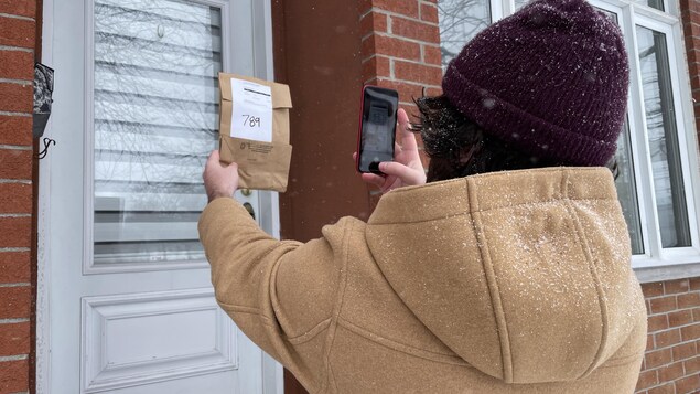Un homme prend en photo un paquet devant une porte d'entrée.