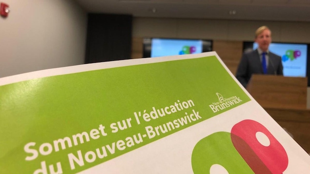La brochure intitulée « Sommet sur l'éducation du Nouveau-Brunswick » et le ministre Cardy dans le fond de la salle.