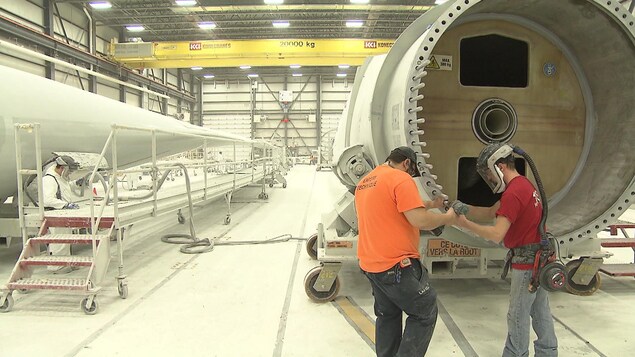 Deux employés travaillent près d'un élément de tour d'éolienne dans l'usine.