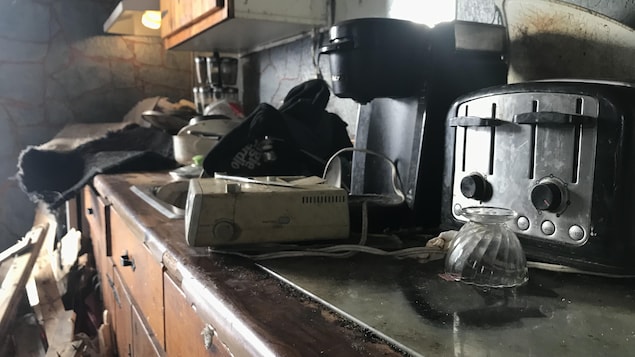 Des appareils électroniques et des objets de toutes sortes traînent sur un comptoir de cuisine souillé.