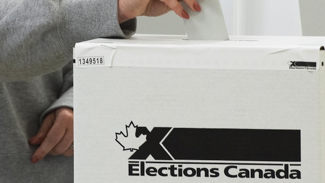 Une femme dépose un bulletin de vote dans une boîte ornée du logo d'Élections Canada.