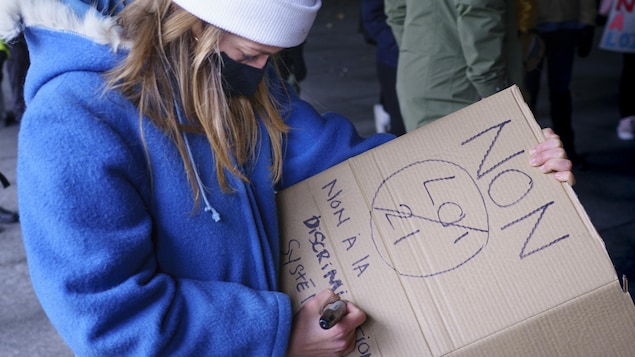 Une femme écrit un message dénonçant la loi 21 sur une pancarte.