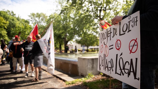 Une personne avec un pancarte contre le projet de loi 97.