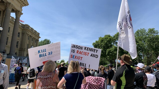 Des manifestants tiennent des pancartes et des drapeaux devant l'Assemblée législative.