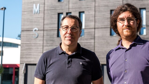 Les deux hommes dehors, devant la bâtisse sur laquelle on peut lire IMS. Les deux hommes dehors, devant la bâtisse sur laquelle on peut lire IMS.