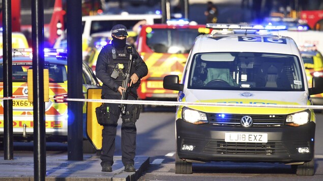 Un policier armé entouré de voitures de police.