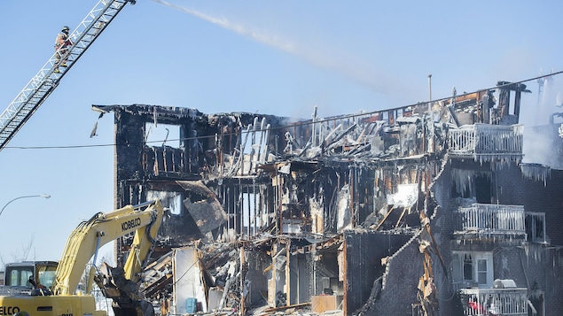 Une pelle mécanique travaille à démolir un bâtiment très gravement endommagé par les flammes.